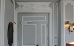 The laconic form of moldings, door trims, complemented by elegant stucco elements of the ceiling Fragment of the living room interior in gray tones with stucco decor