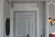 The laconic form of moldings, door trims, complemented by elegant stucco elements of the ceiling Fragment of the living room interior in gray tones with stucco decor