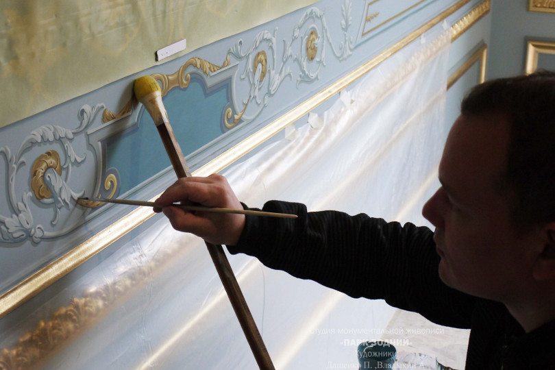 Под пленкой находится текстильные обои такого же колорита как и роспись Художник выполняет роспись на стене