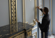 Позолотчик вызолачивает архитектурное зеркало Мастер позолоты гипсовой лепнины