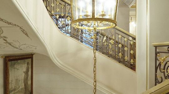 To the light basic tone of the staircase, gilding of details, alfrey painting and a large stylized painting are subtly added Staircase in a country mansion with painting and gilding